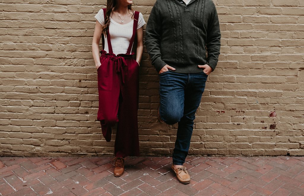 Couple leaning casually against yellow brick wall outside of Lancaster Central Market in Downtown Lancaster, PA