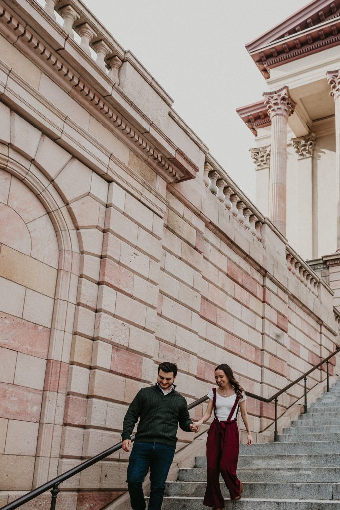 Engaged couple walking down the steps hand in hand on the steps of the Lancaster County Courthouse in Downtown Lancaster, PA