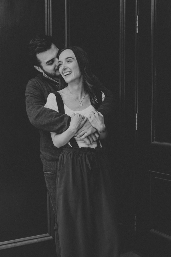 Engaged couple holding each other in a hug as they laugh and share candid moments outside of Excelsior in Downtown Lancaster, PA