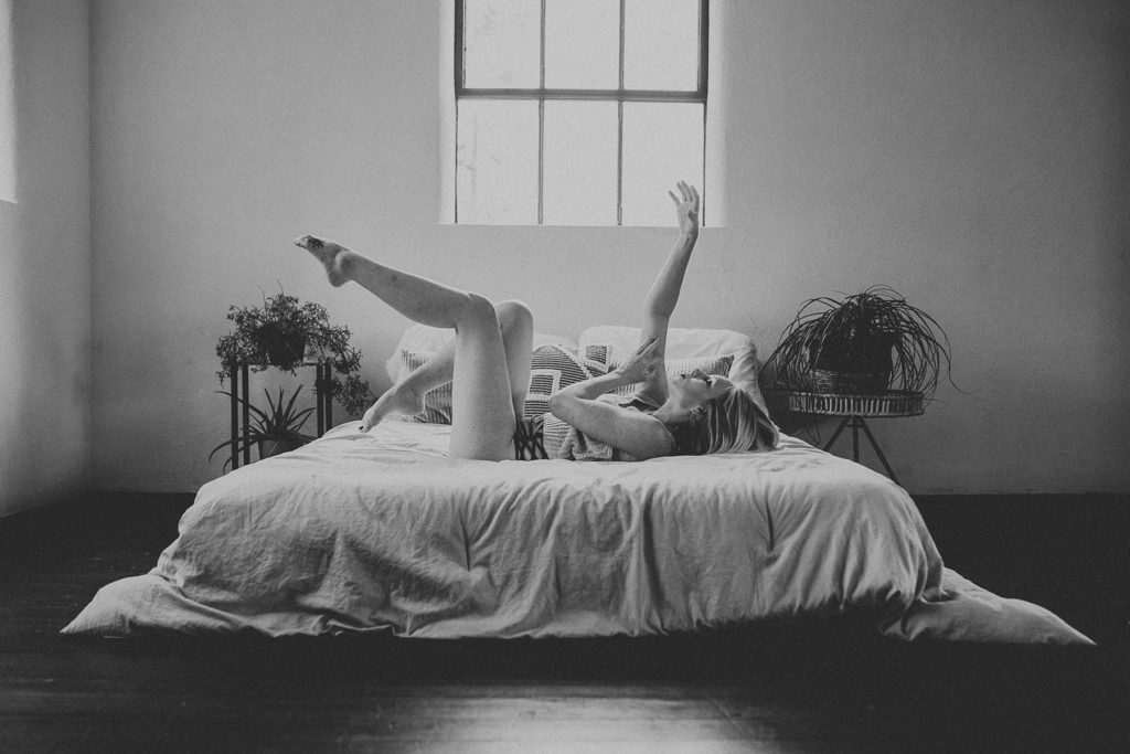 Female on bed moving arms and legs gracefully in feminine way during boudoir session in Downtown York, PA