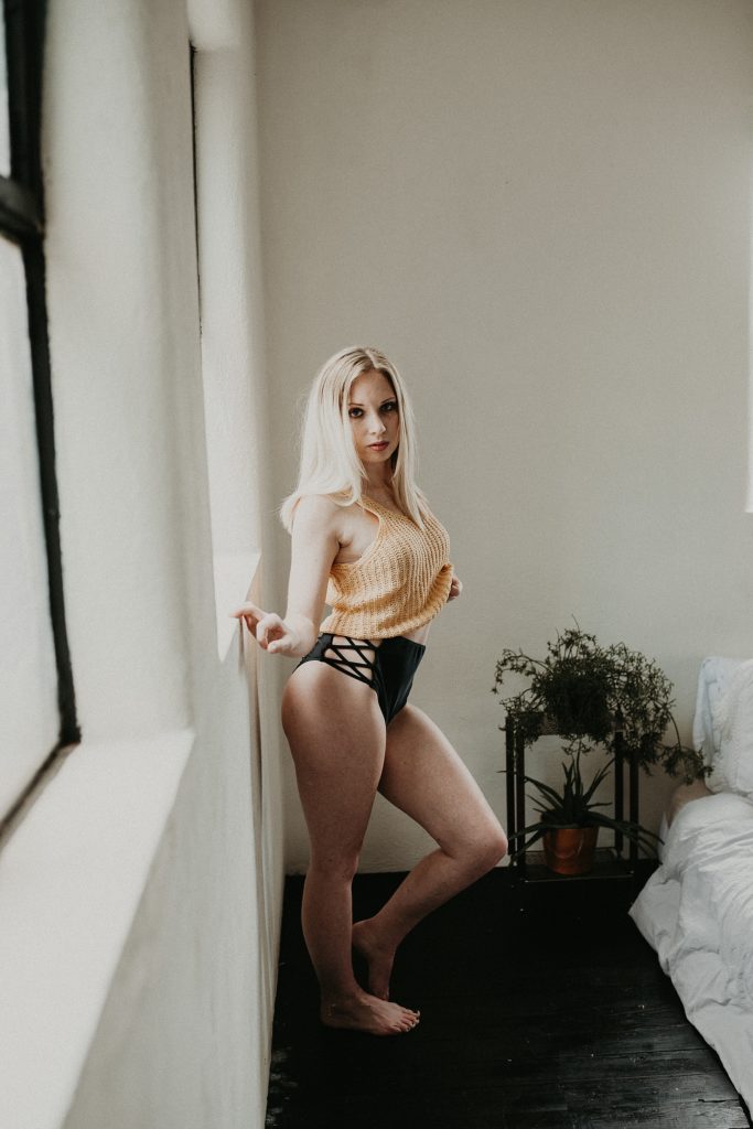 Soft light through wonder filters through as women stands with hips out accentuating curves during boudoir session in Downtown York, PA