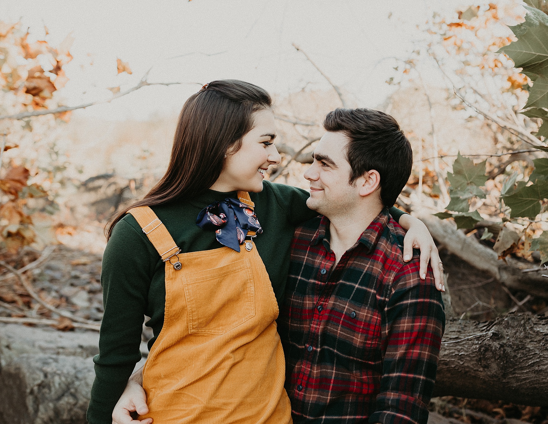 Girl sitting in guys lap with her arms wrapped around his neck as they gaze into each others eyes