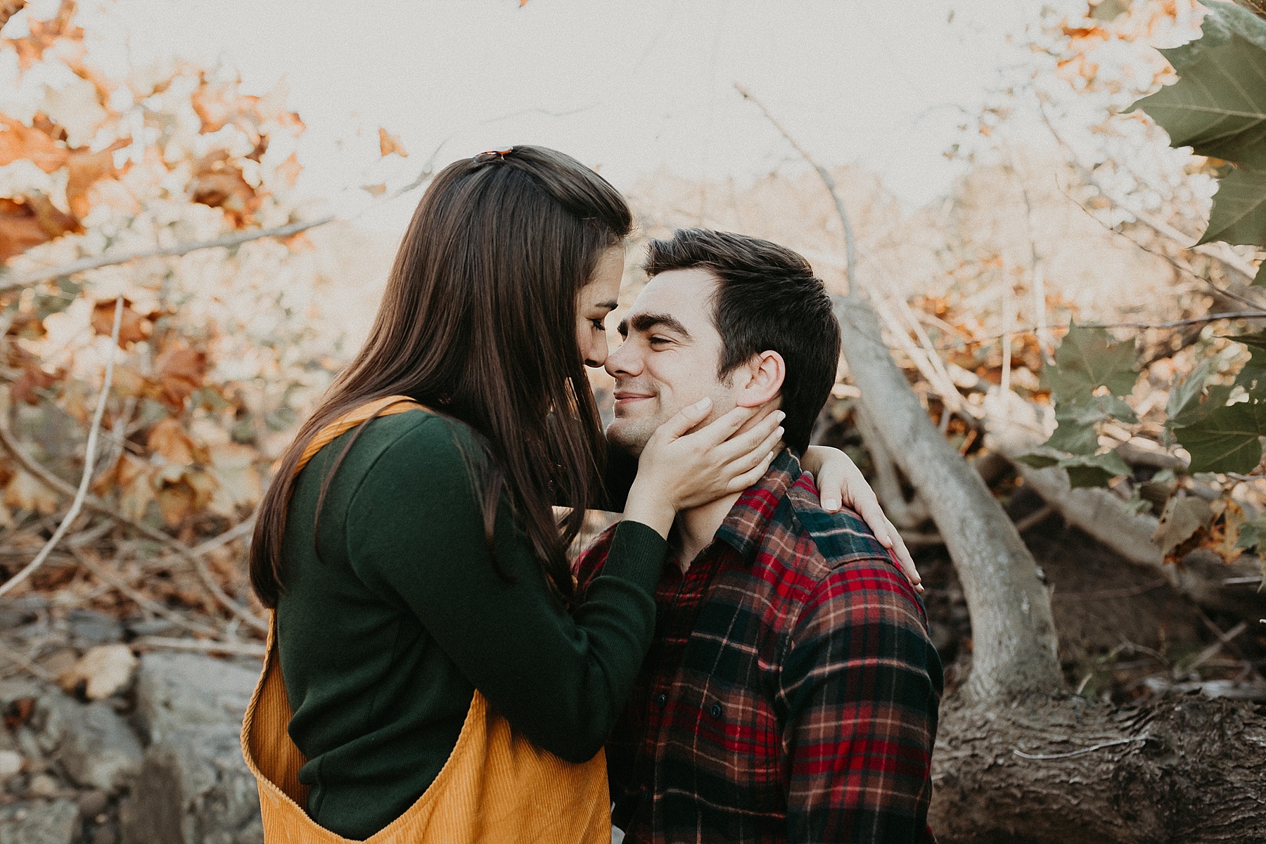 Girl sitting in guys lap with her hands against his cheek as they gaze into each others eyes