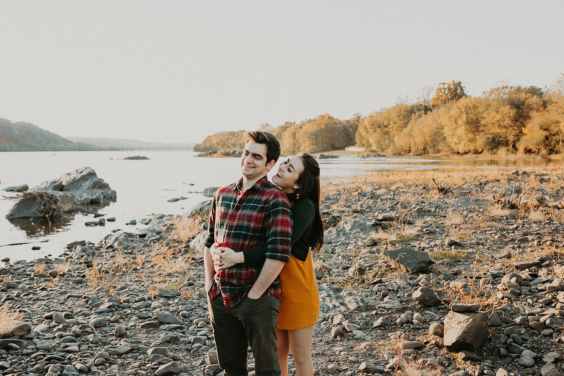 Girl standing behind guy with her arms wrapped around his wait leaning into him as she whispers in his ear while smiling