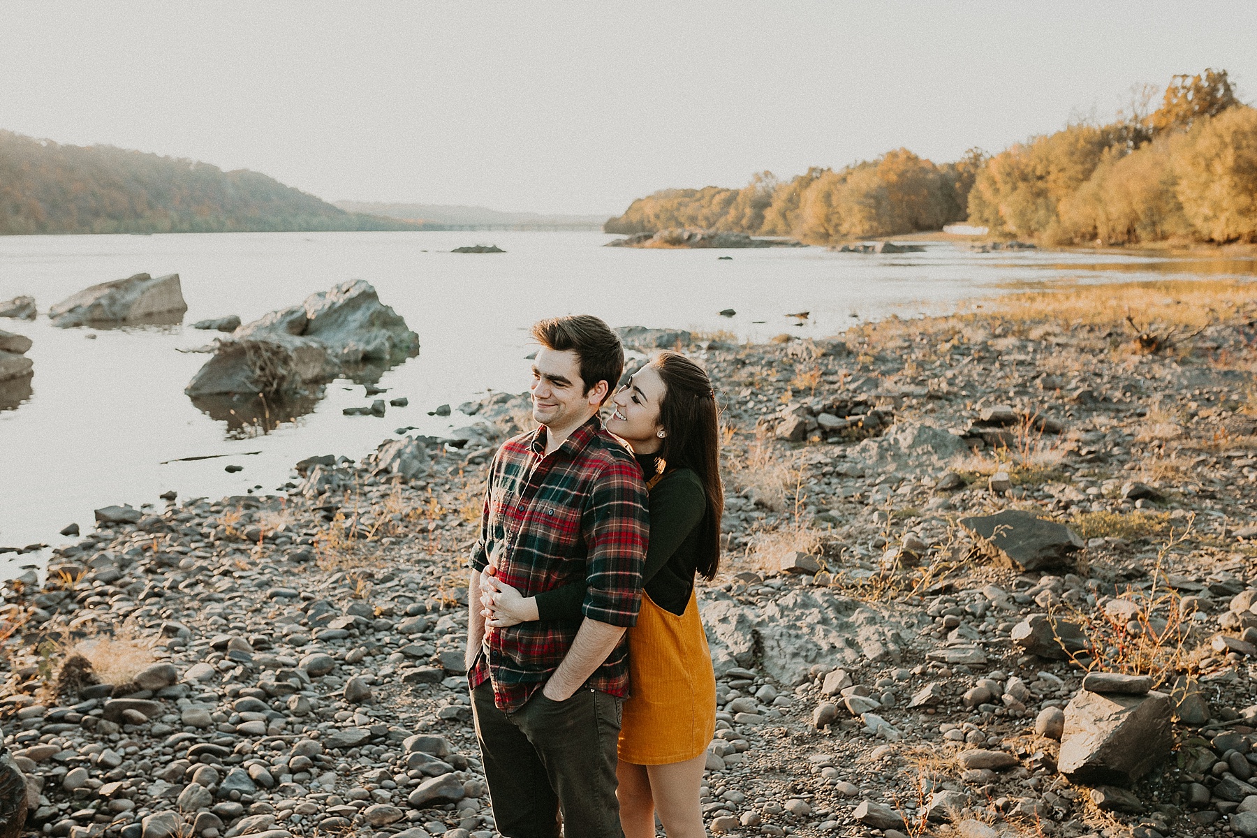 Girl standing behind guy with her arms wrapped around his wait leaning into him as she whispers in his ear while smiling