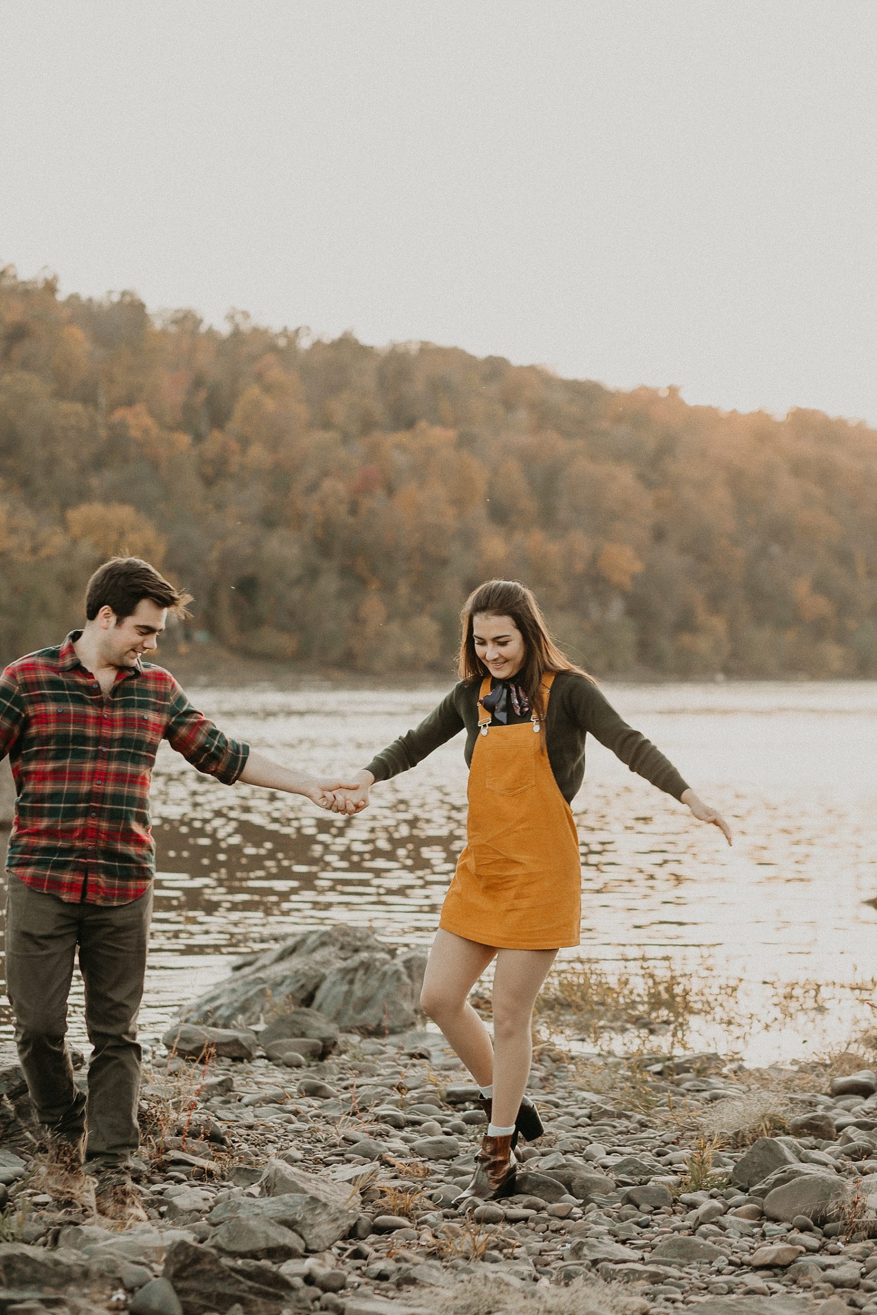 Engaged couple holding hands as they walk playfully along the Susquehanna River laughing and having fun