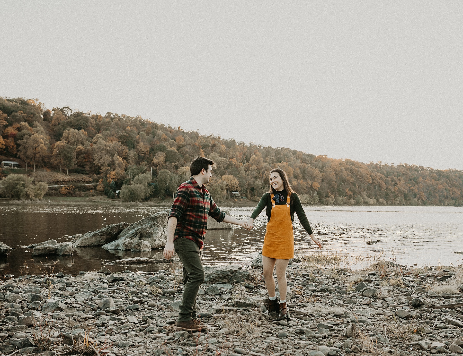 Engaged couple holding hands as they walk playfully along the Susquehanna River laughing and having fun