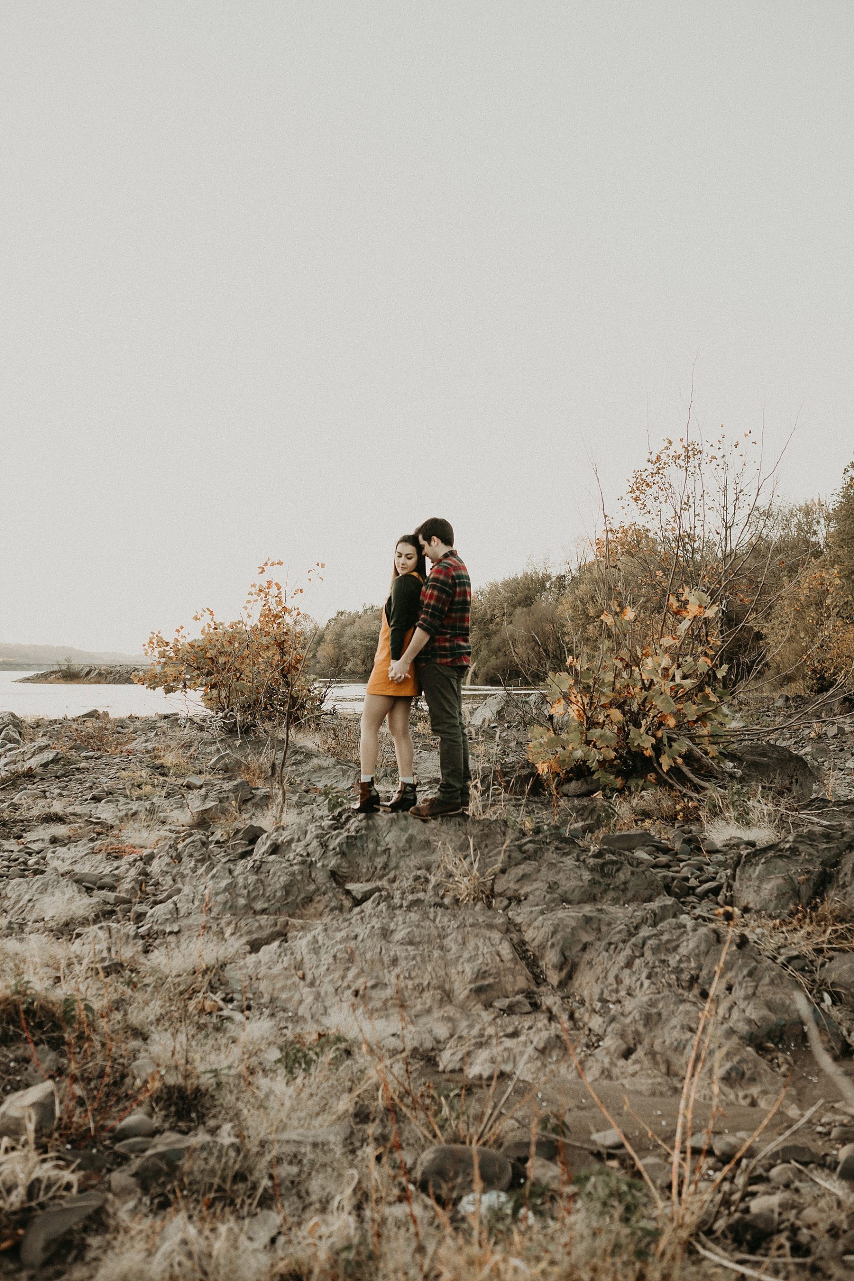 Couple holding hands as they walk along the top of a rocky ledge as the sun sets in front of them