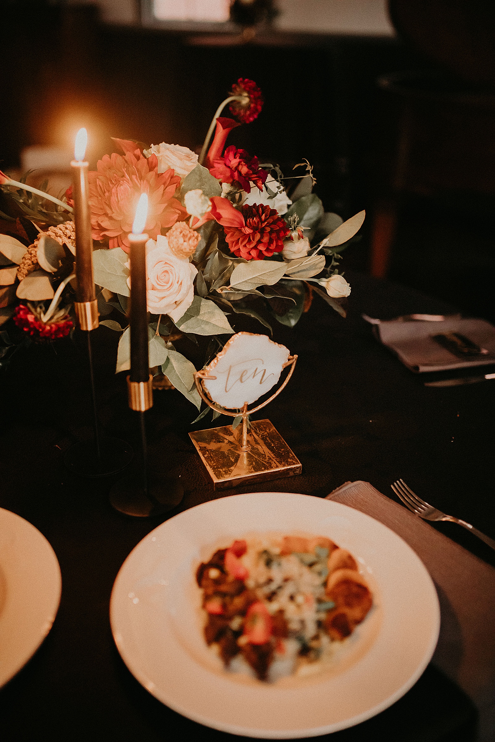 Candlelit reception table set with hand lettered place cards and a large floral centerpiece.