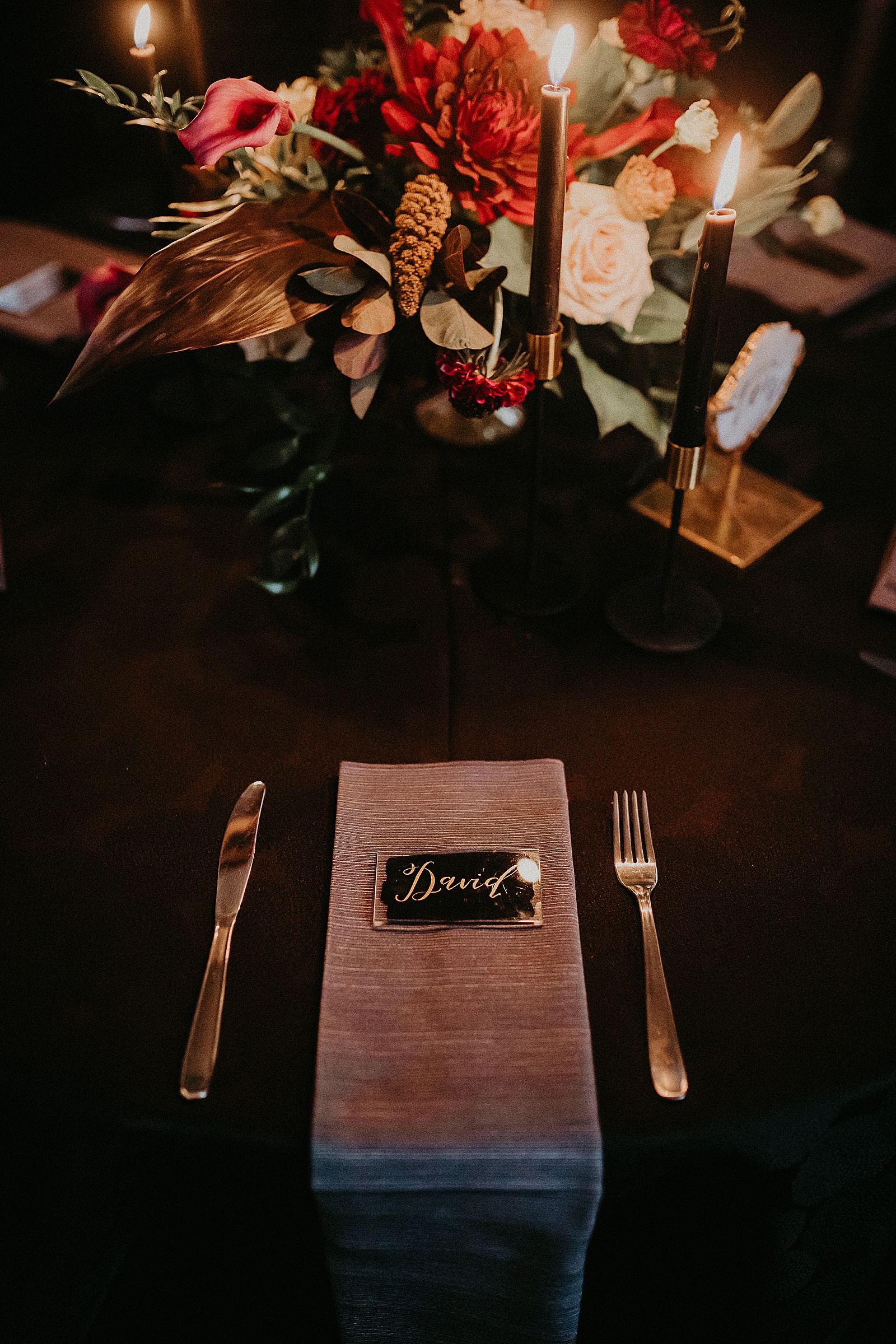 Candlelit reception table set with hand lettered place cards and a large floral centerpiece.