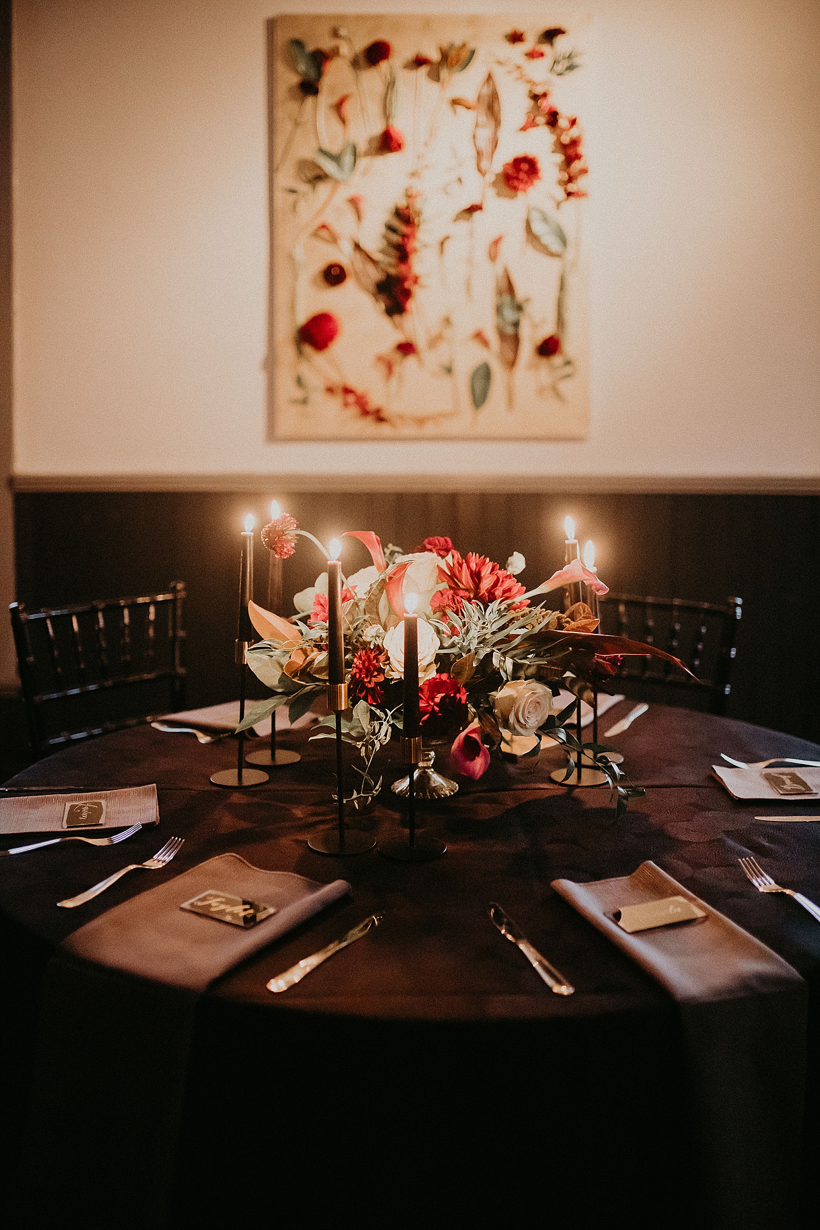 Candlelit reception table set with hand lettered place cards and a large floral centerpiece.