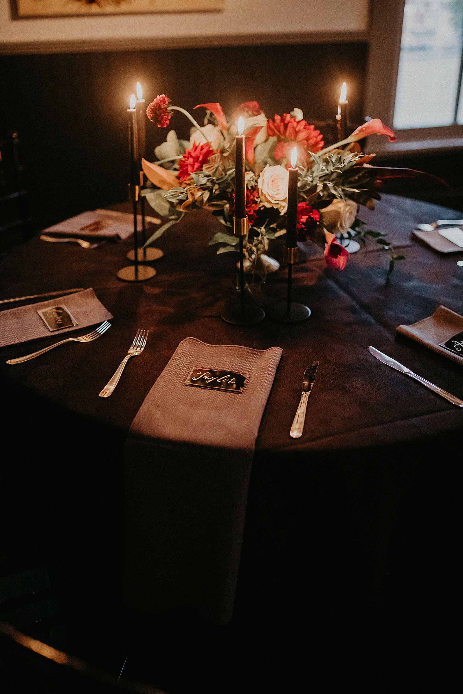 Candlelit reception table set with hand lettered place cards and a large floral centerpiece.