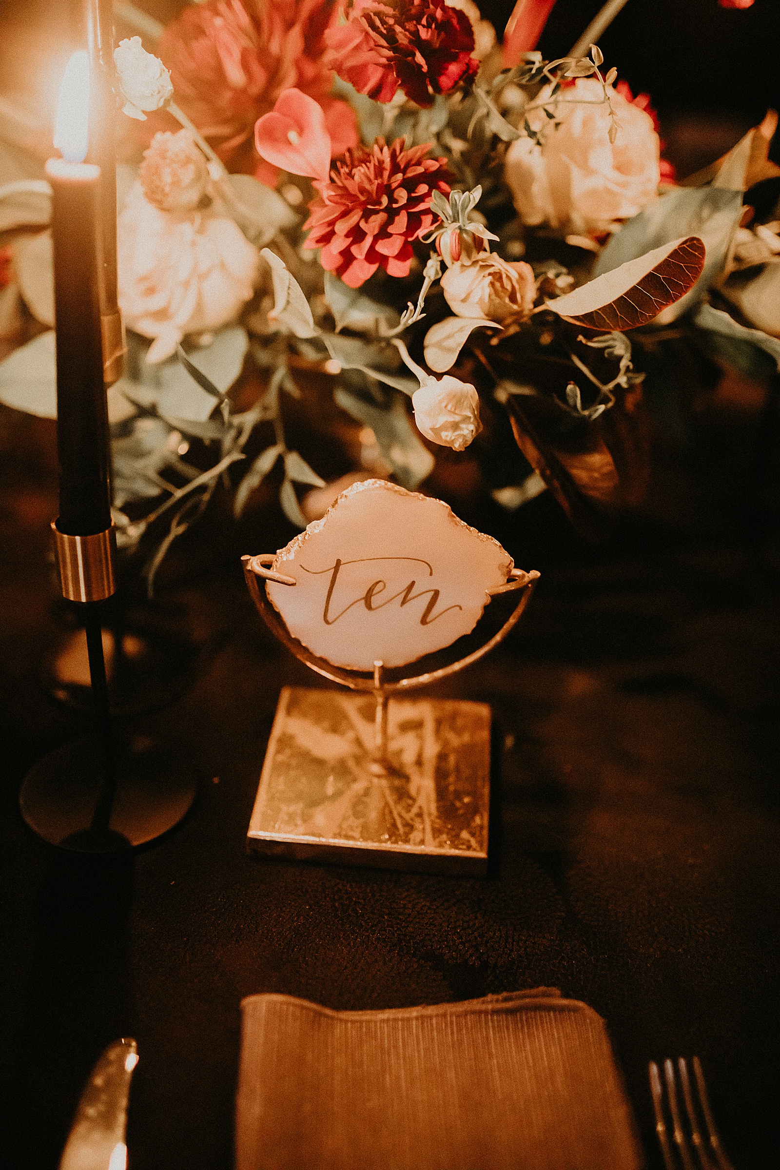 Candlelit reception table set with hand lettered place cards and a large floral centerpiece.