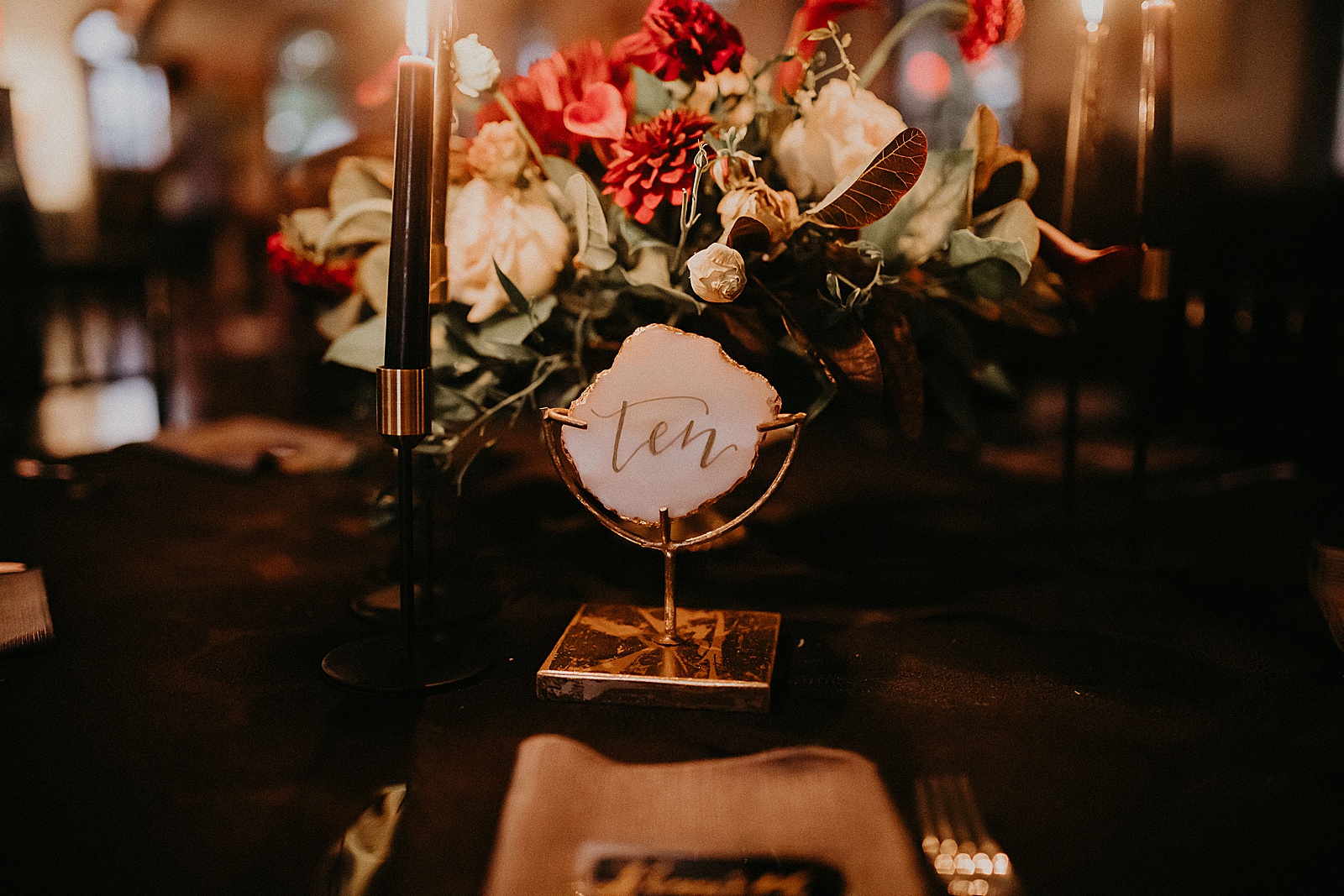 Candlelit reception table set with hand lettered place cards and a large floral centerpiece.